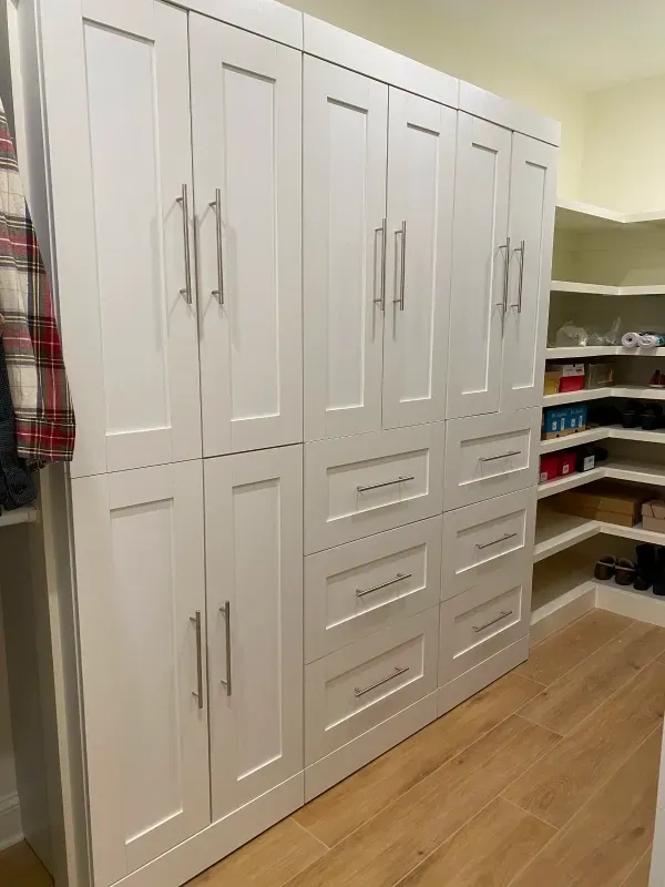 White custom closet with cabinets and drawers, light wood floor.