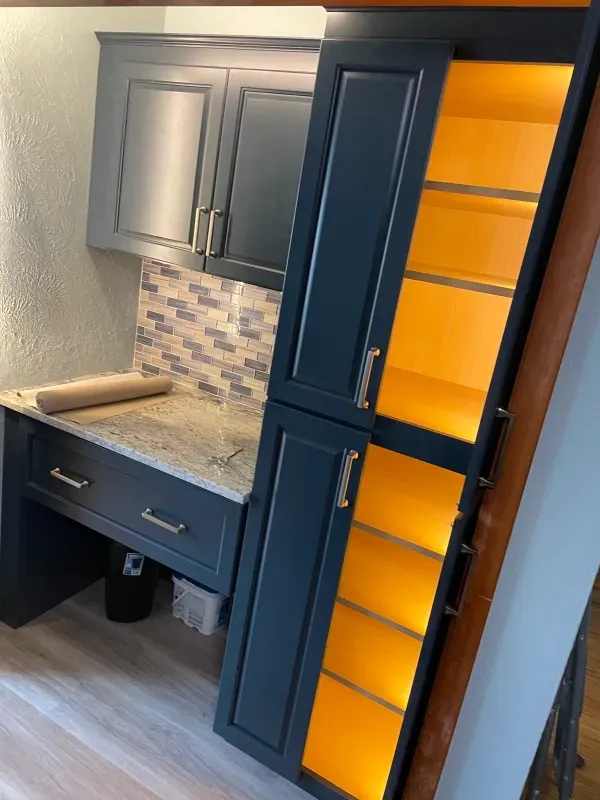 Blue cabinets and pantry with lit shelves; kitchen corner with counter and tiled backsplash.