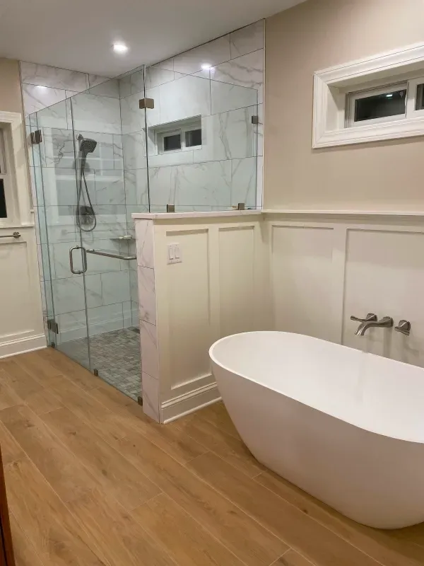 Modern bathroom with a glass shower, freestanding tub, and light wood flooring.