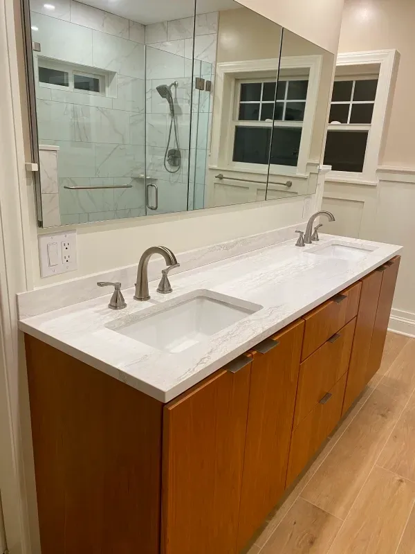 Bathroom vanity with two sinks, light countertop, wood cabinets, large mirror, and white walls.