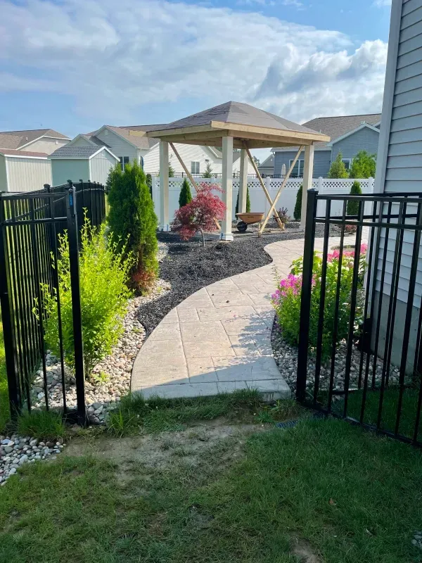 Black fenced yard with stone pathway leading to a gazebo, surrounded by landscaping.