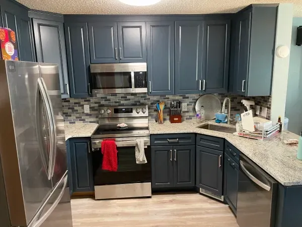 Blue kitchen cabinets with stainless steel appliances, gray countertops, and light flooring.