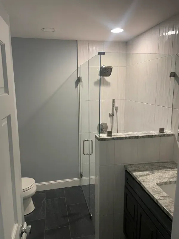 Modern bathroom with a glass shower, white tile, dark vanity, and blue walls.