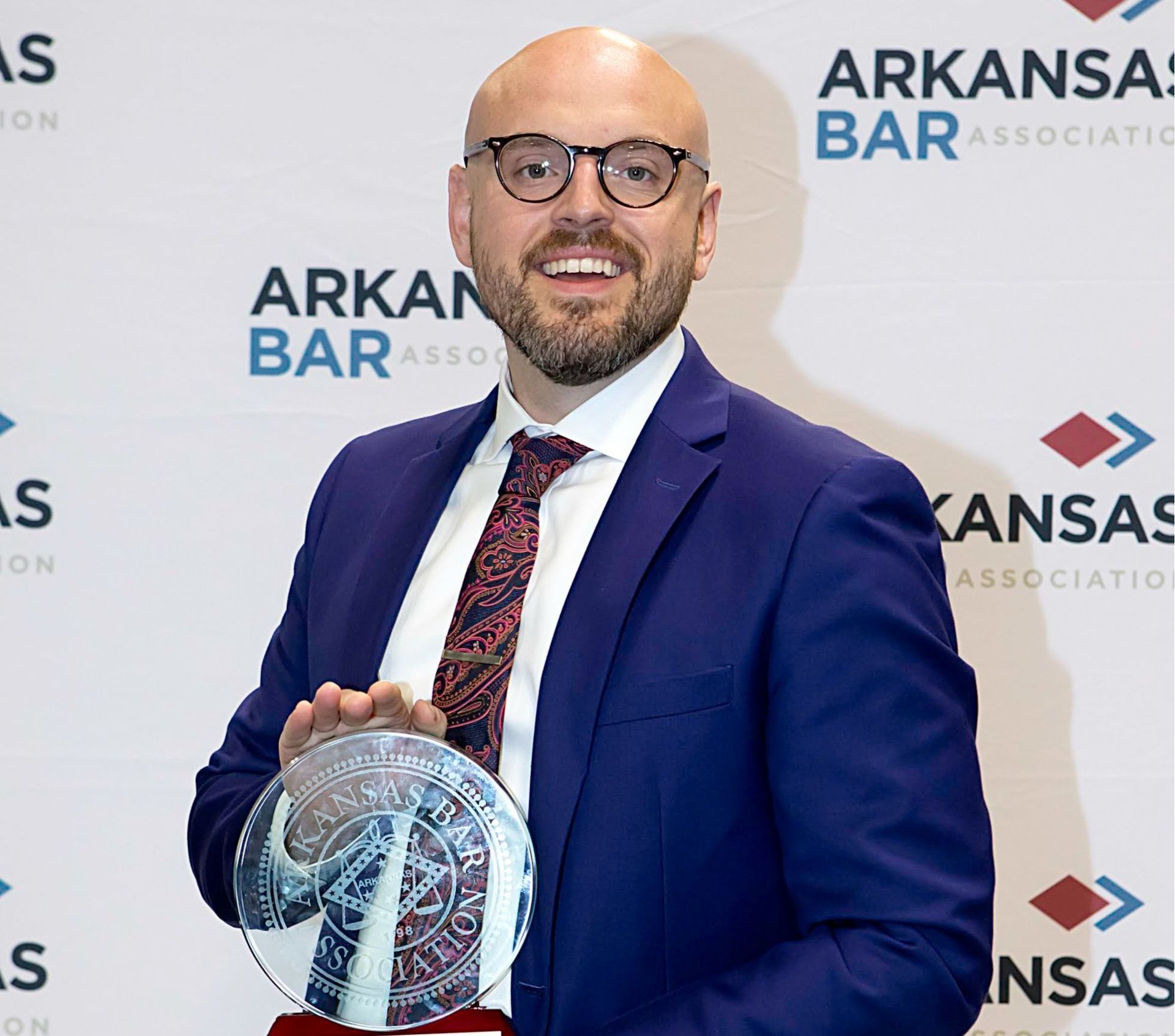 A man in a blue suit and tie is holding a trophy