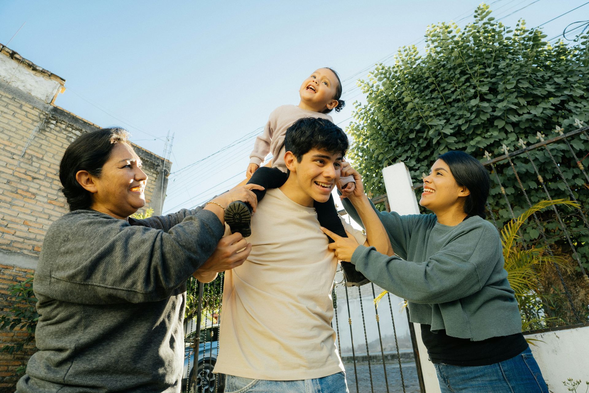 Two women are holding a child on a man 's shoulders.