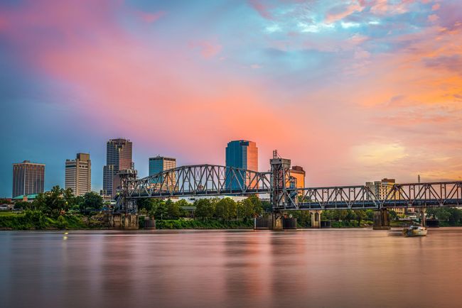 A bridge over a river with a city skyline in the background at sunset.