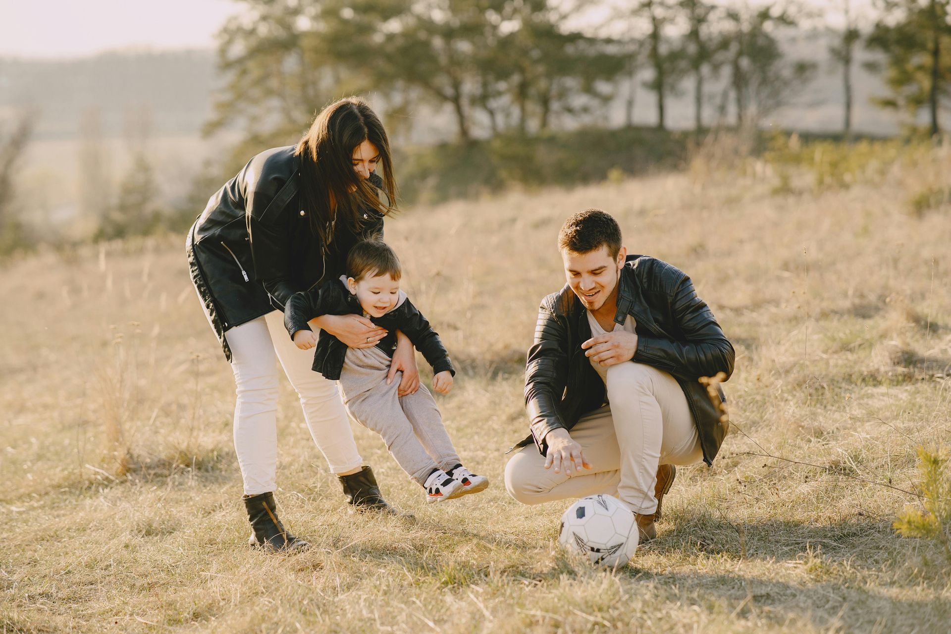 A family is playing with a soccer ball in a field.