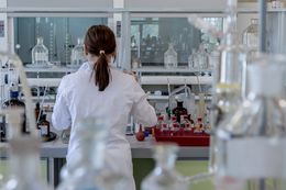 Wetenschapper in een witte laboratoriumjas aan het werk aan een laboratoriumtafel met glaswerk en apparatuur.