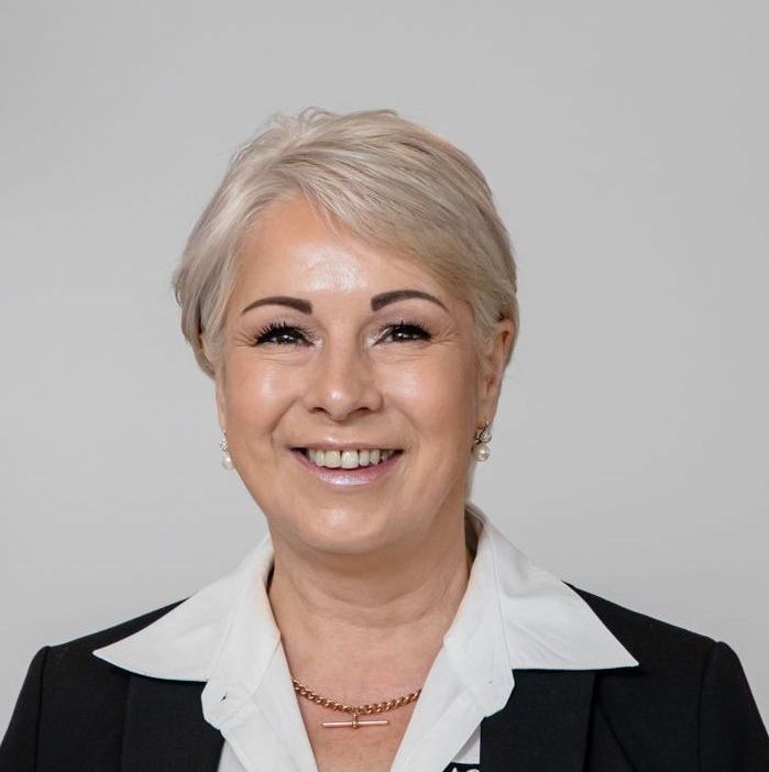 A woman wearing a white shirt and a black jacket smiles for the camera