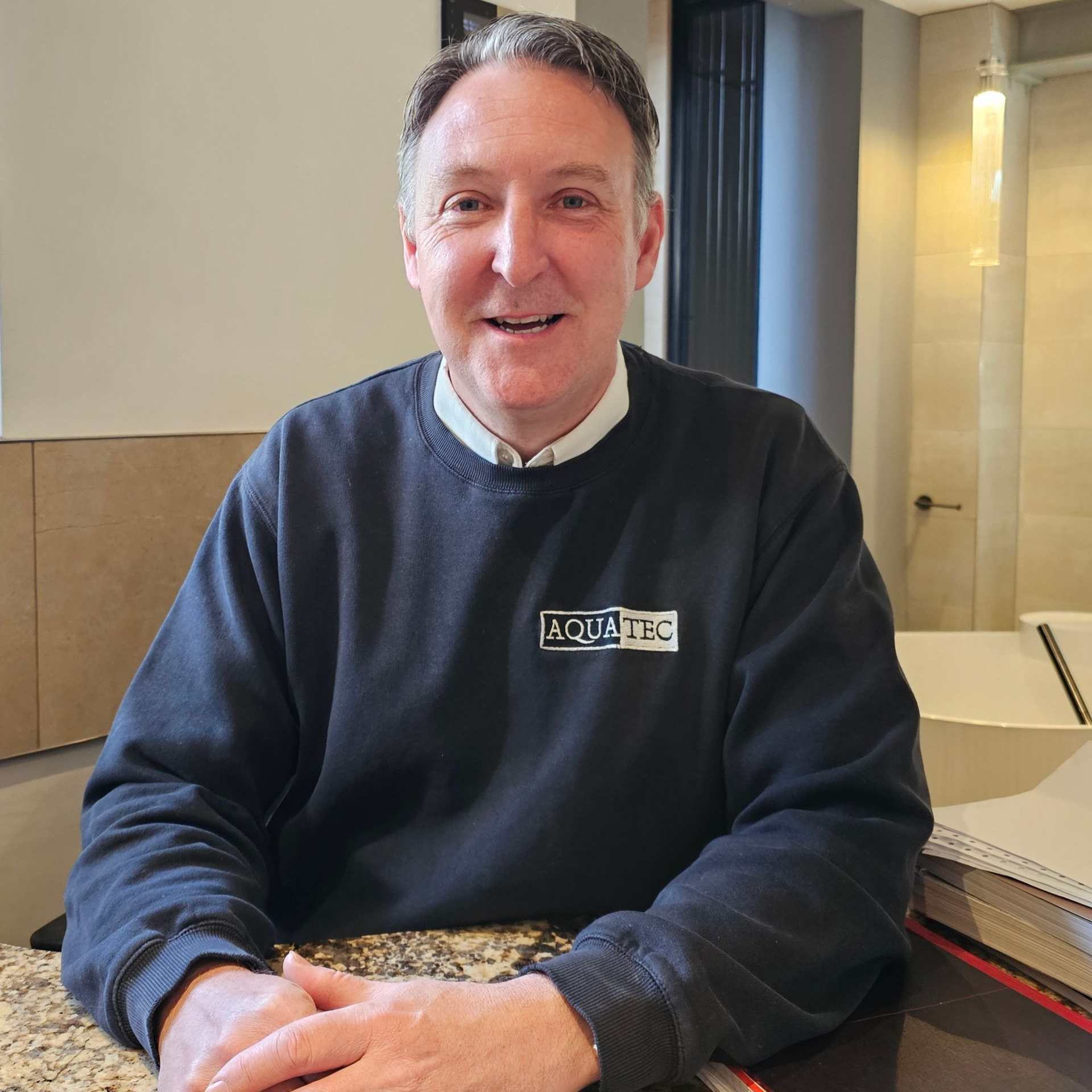 A man wearing a black Aquatec jumper smiles for the camera