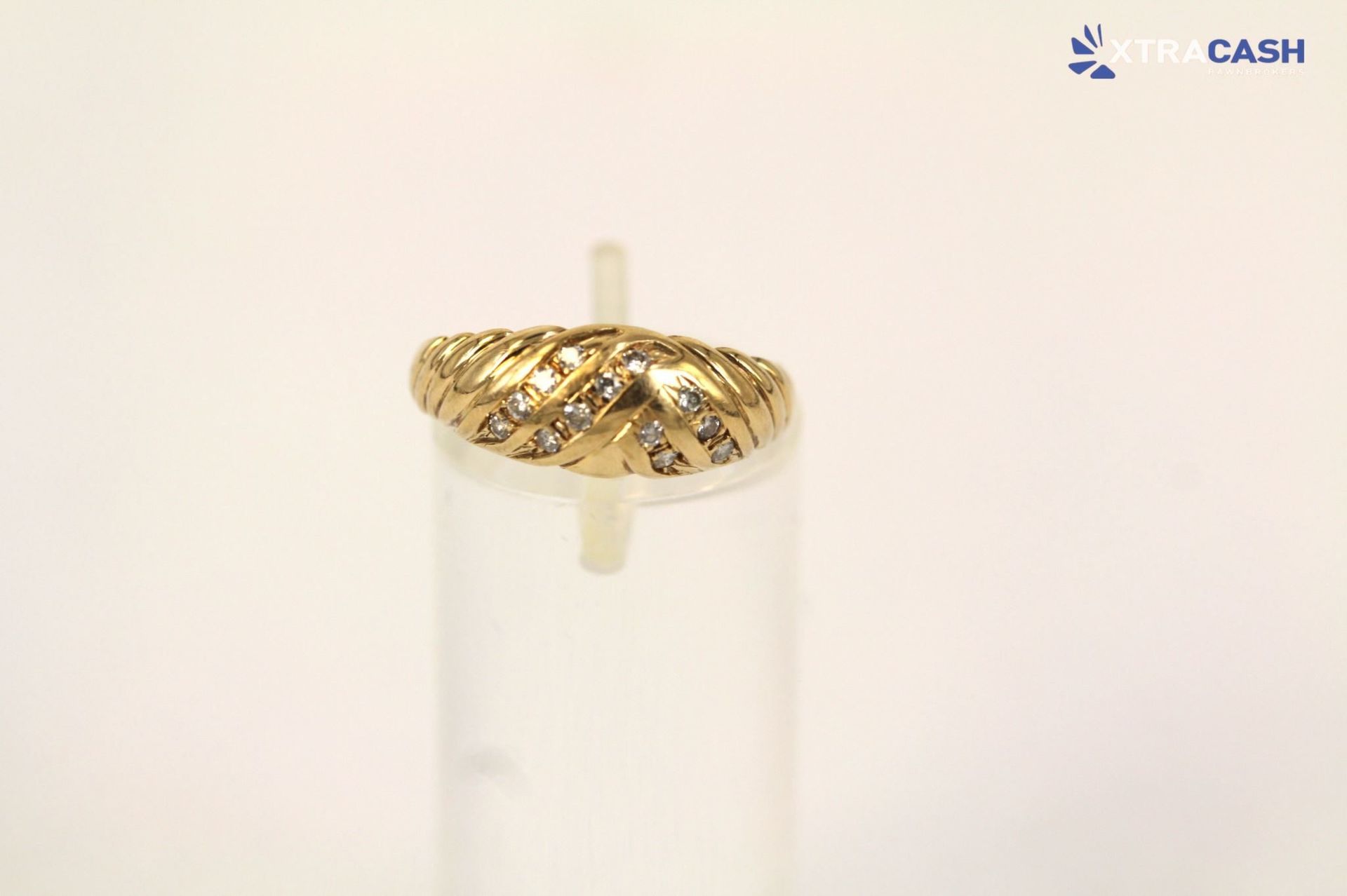 Gold patterned ring on a clear cylindrical stand against a white background