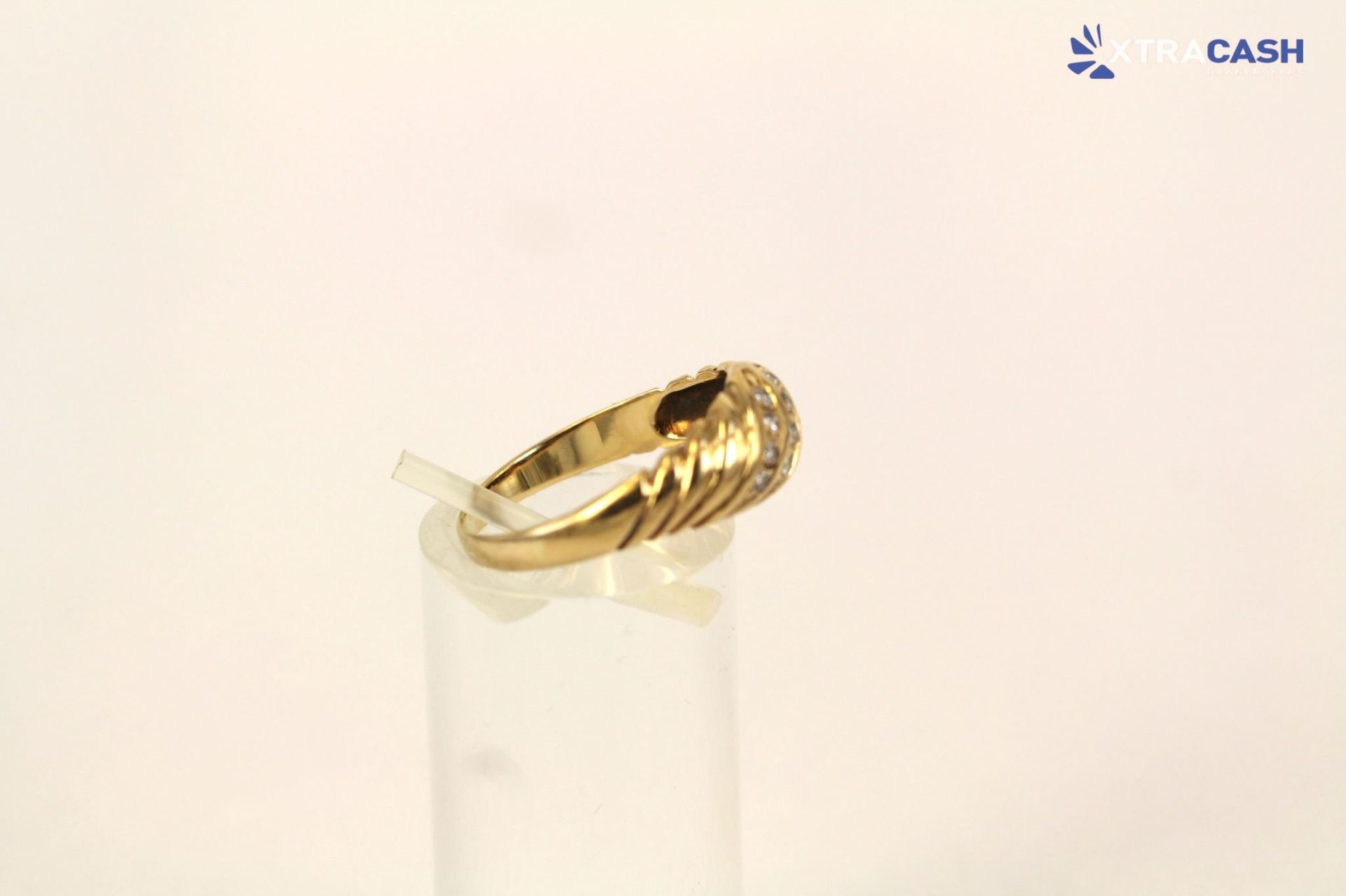 Gold patterned ring on a clear cylindrical stand against a white background