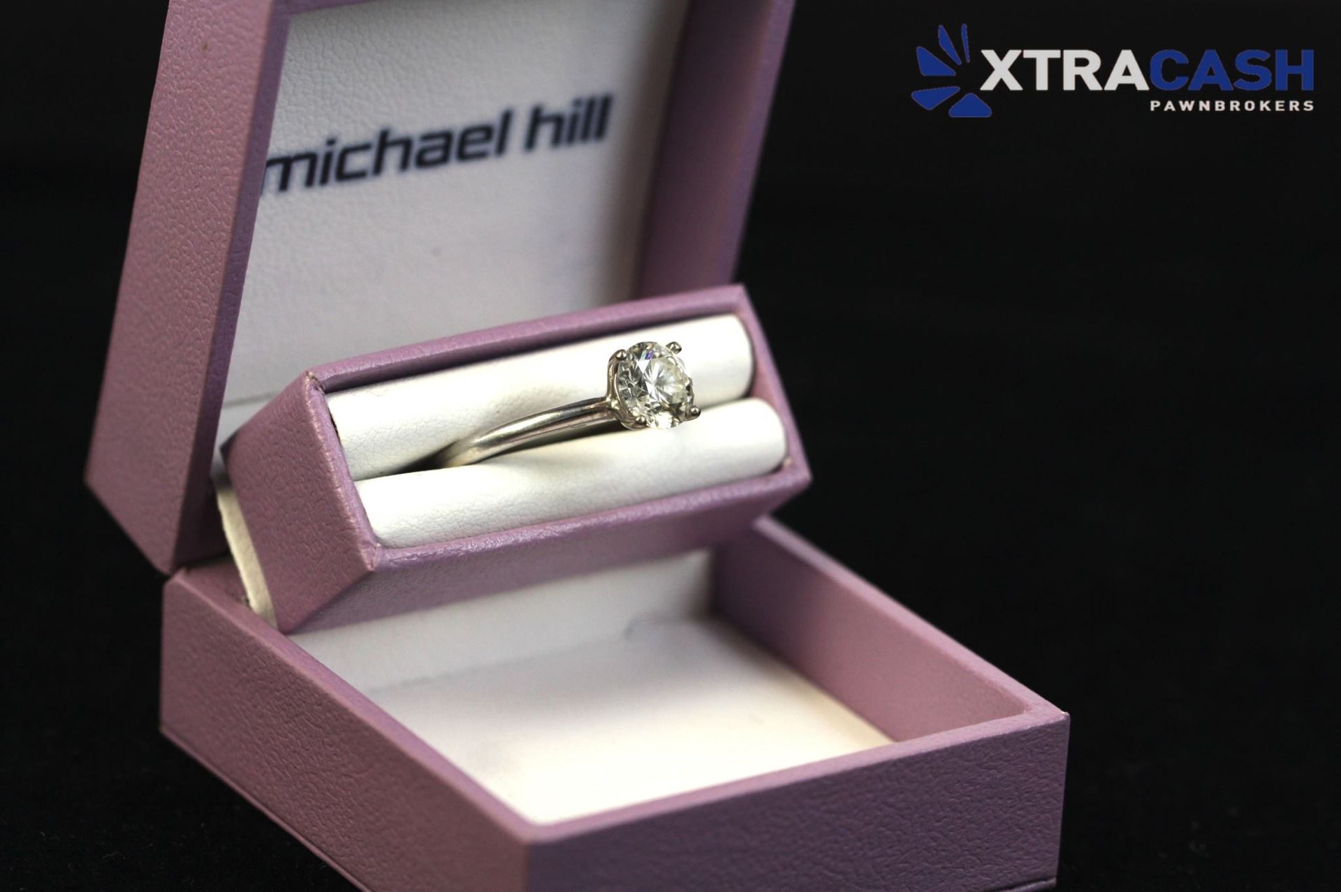 Purple jewelry box displaying a silver ring on a white cushion, with Michael Hill branding inside the lid
