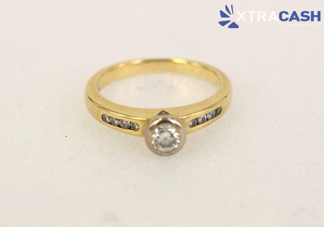 Gold ring with central clear gemstone and small side stones on a white background