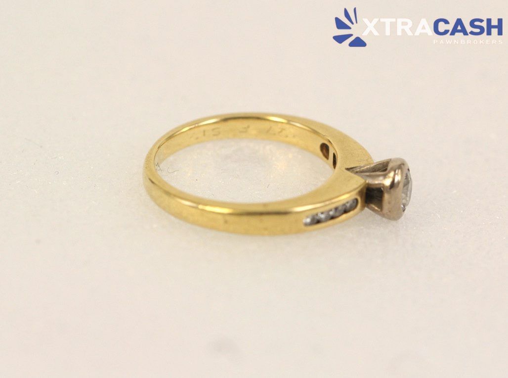 Gold ring with central clear gemstone and small side stones on a white background