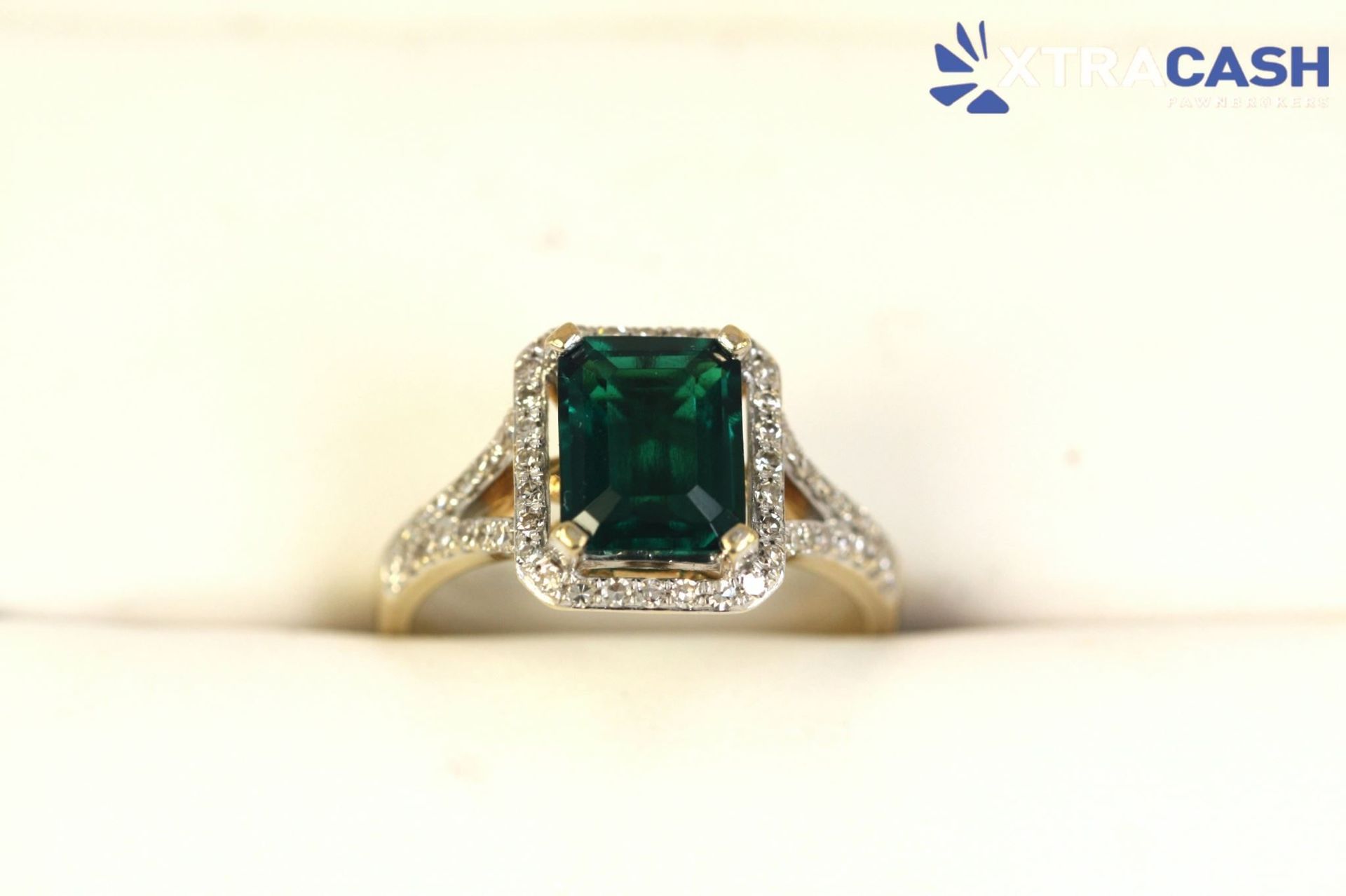 XTRA CASH logo above a gold ring with a green gemstone on a white background