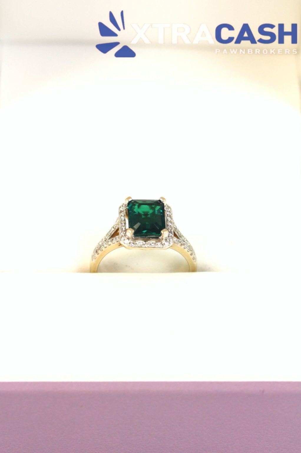 XTRA CASH logo above a gold ring with a green gemstone on a white background