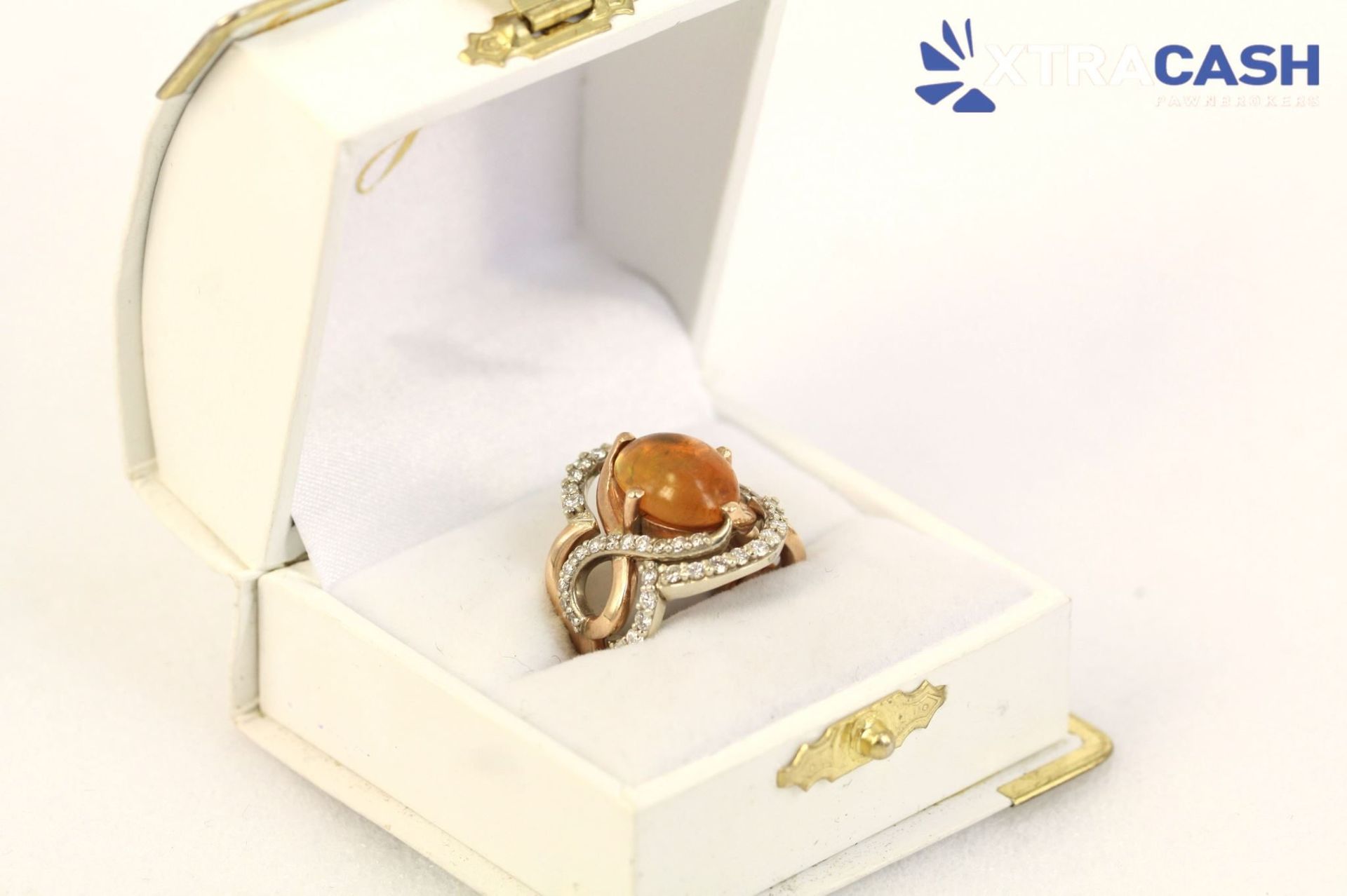 Ring in an open cream jewelry box with a peach stone, CASH logo in the corner