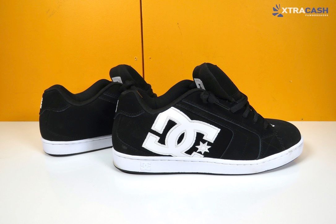Black DC sneakers with white logo and soles on a white surface against a yellow background