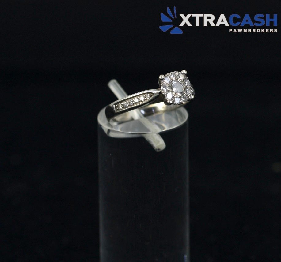 Diamond ring displayed on a black stand against a dark background, with XtraCash logo in the corner