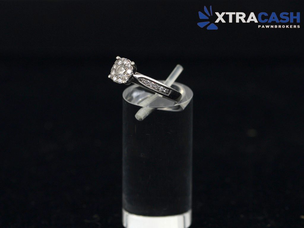 Diamond ring displayed on a black stand against a dark background, with XtraCash logo in the corner