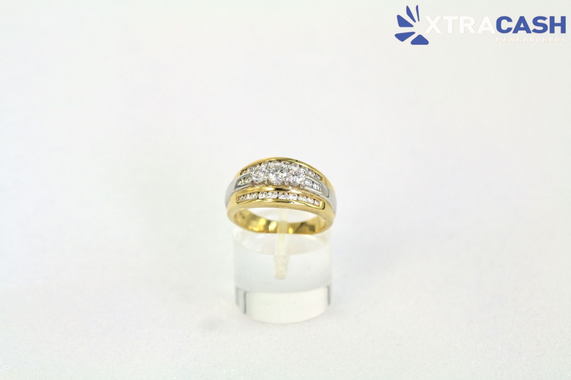 Gold ring with diamond accents on a clear display stand against a white background