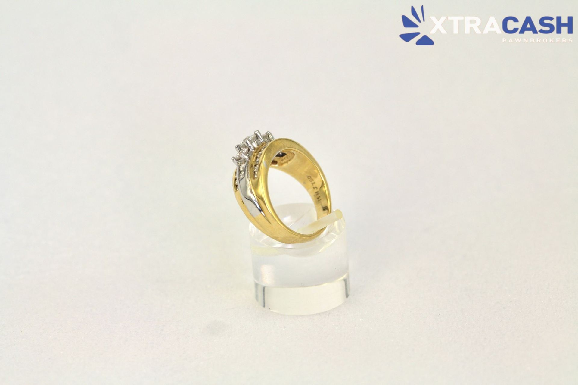 Gold ring with diamond accents on a clear display stand against a white background