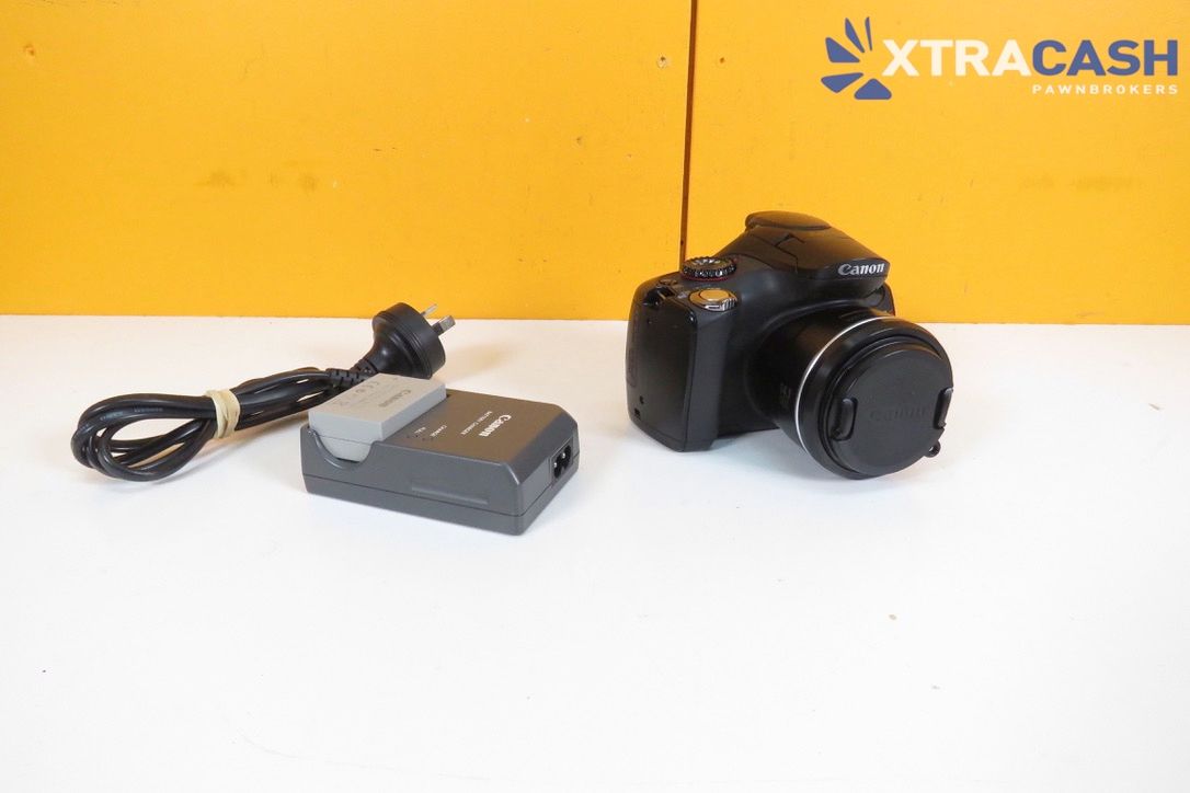 Black camera with attached lens beside a charger on a white surface against a yellow background