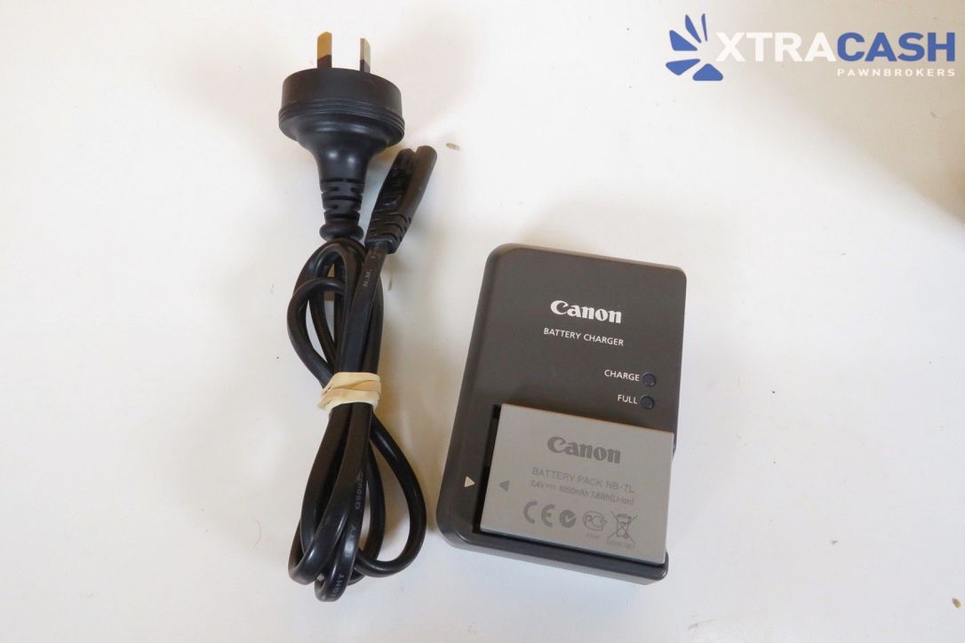 Black camera with attached lens beside a charger on a white surface against a yellow background