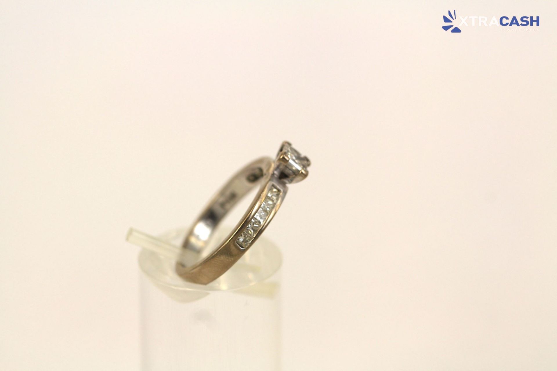 Silver diamond ring displayed on a stand against a plain light background.