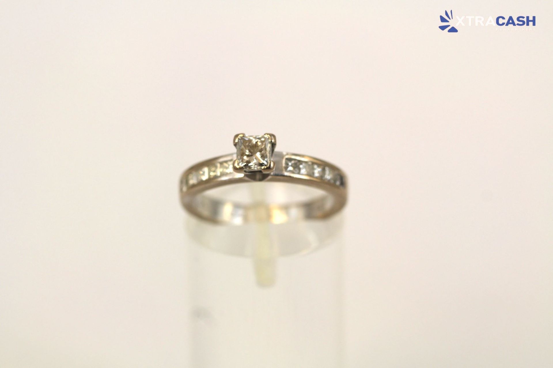 Silver diamond ring displayed on a stand against a plain light background.