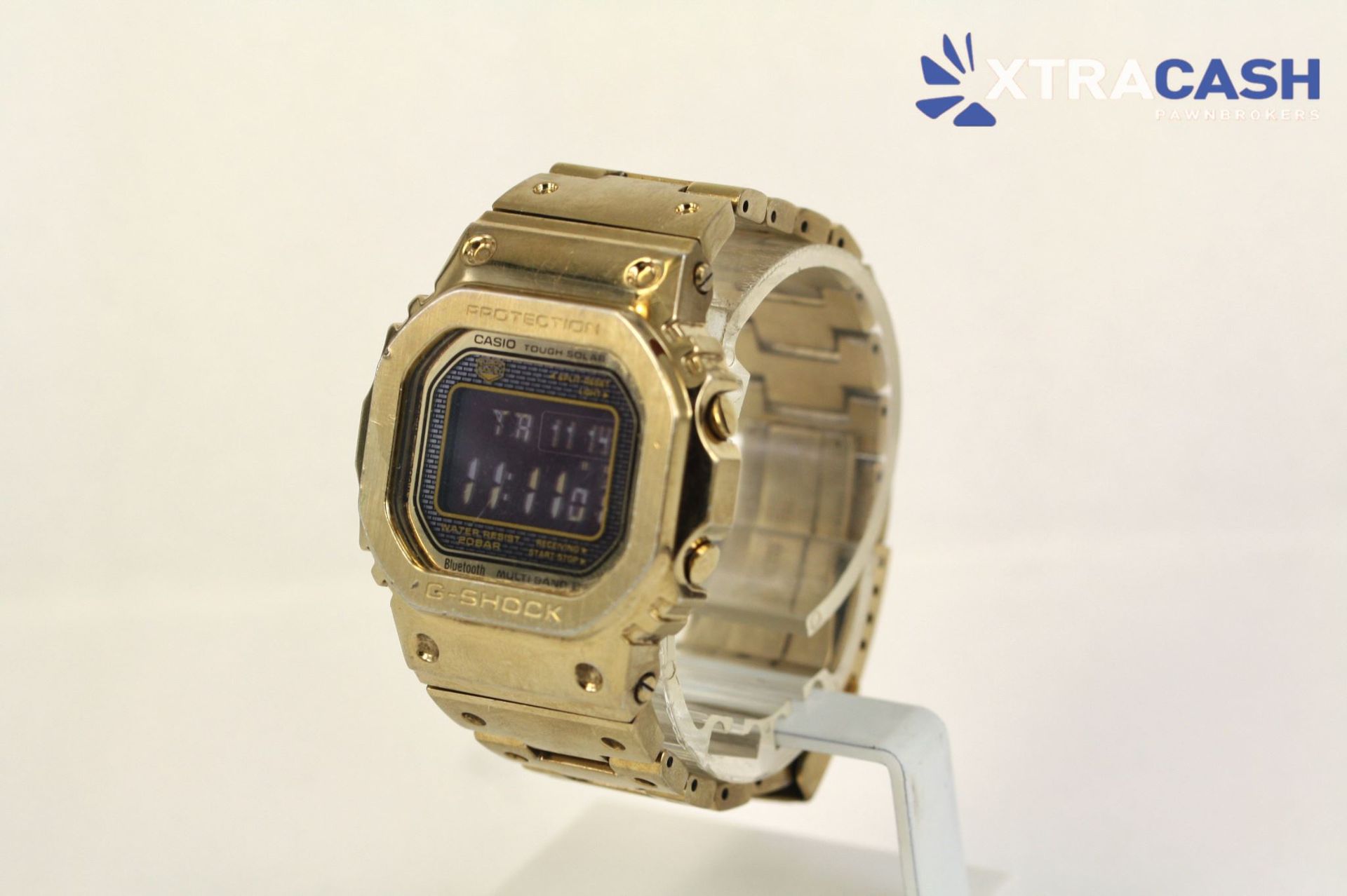 Gold digital wristwatch on a display stand with a transparent strap, set against a light background.