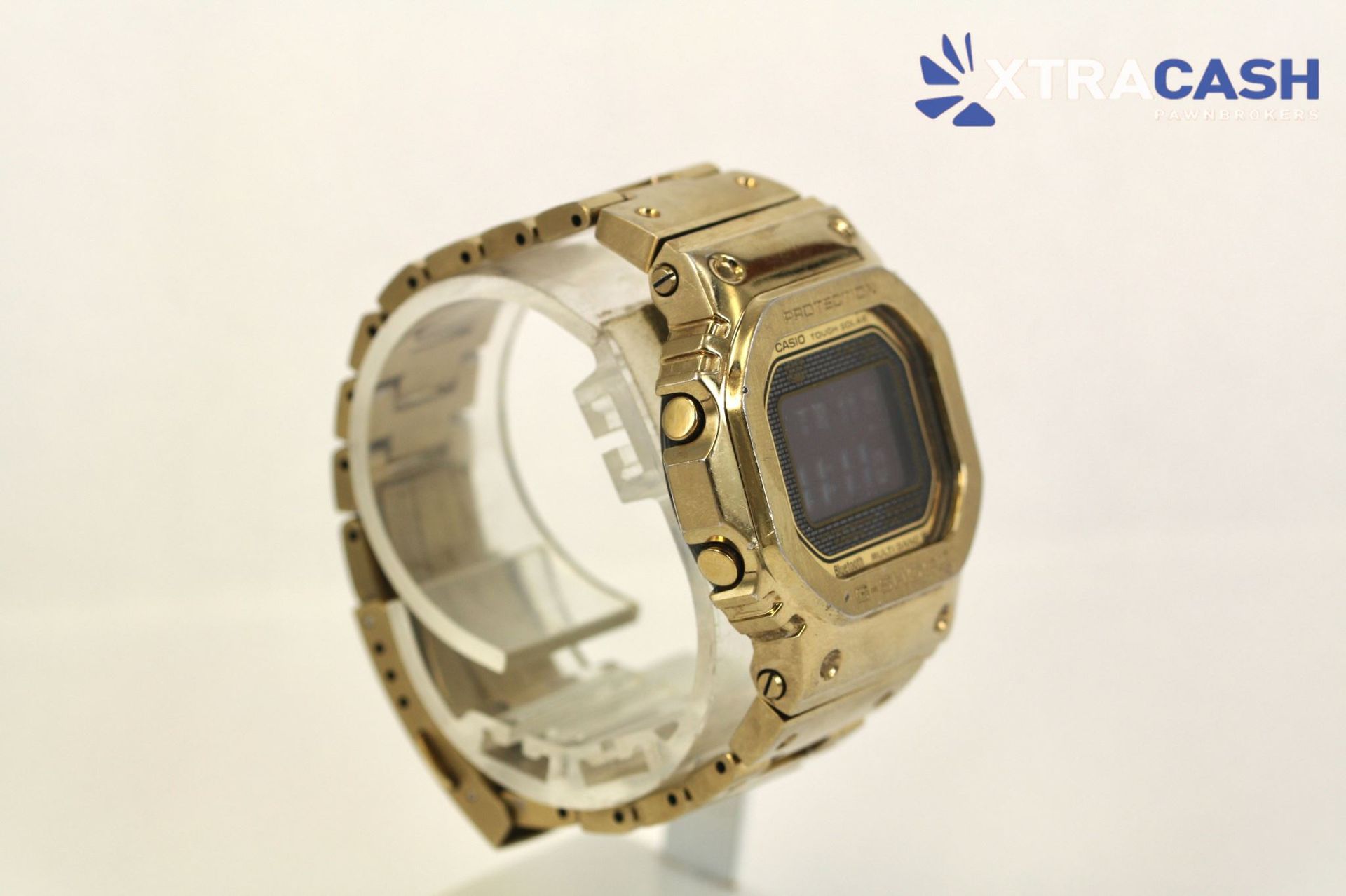 Gold digital wristwatch on a display stand with a transparent strap, set against a light background.