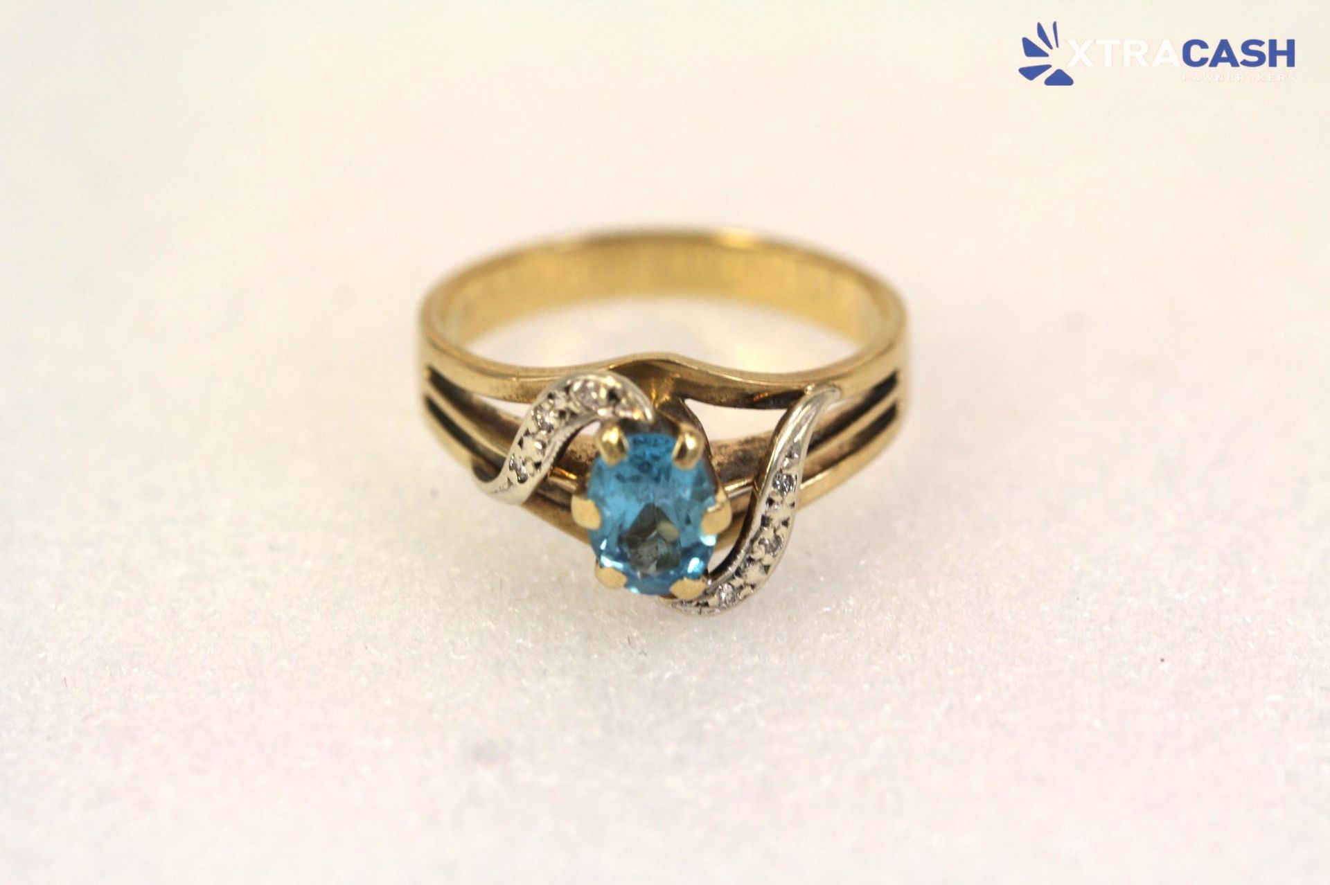 Gold ring with a blue gemstone on a white display stand