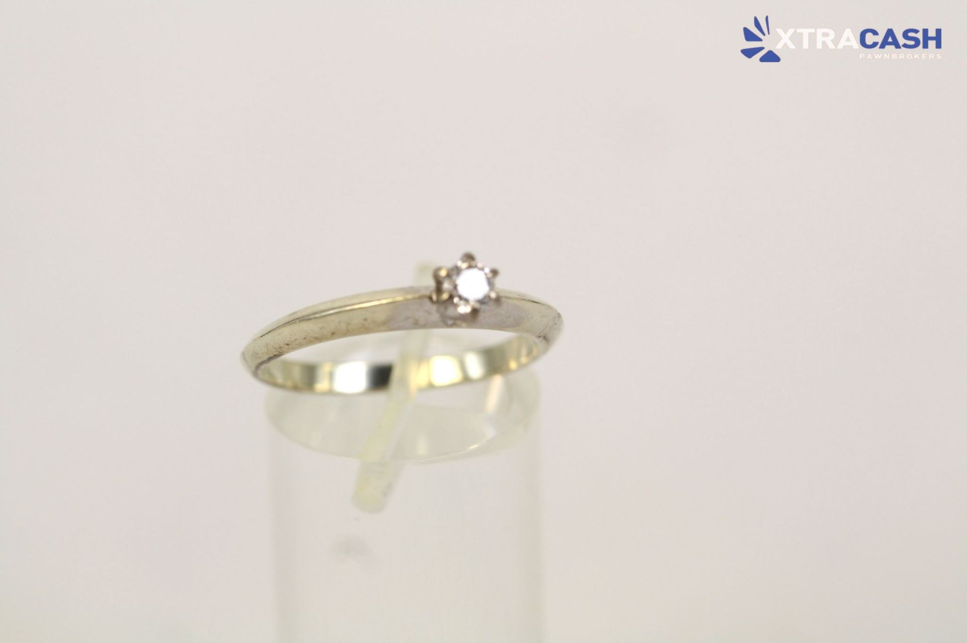 Gold ring with a small star-shaped diamond on a clear stand against a white background