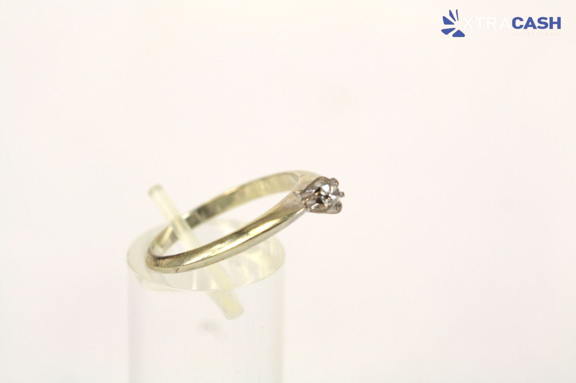 Gold ring with a small star-shaped diamond on a clear stand against a white background