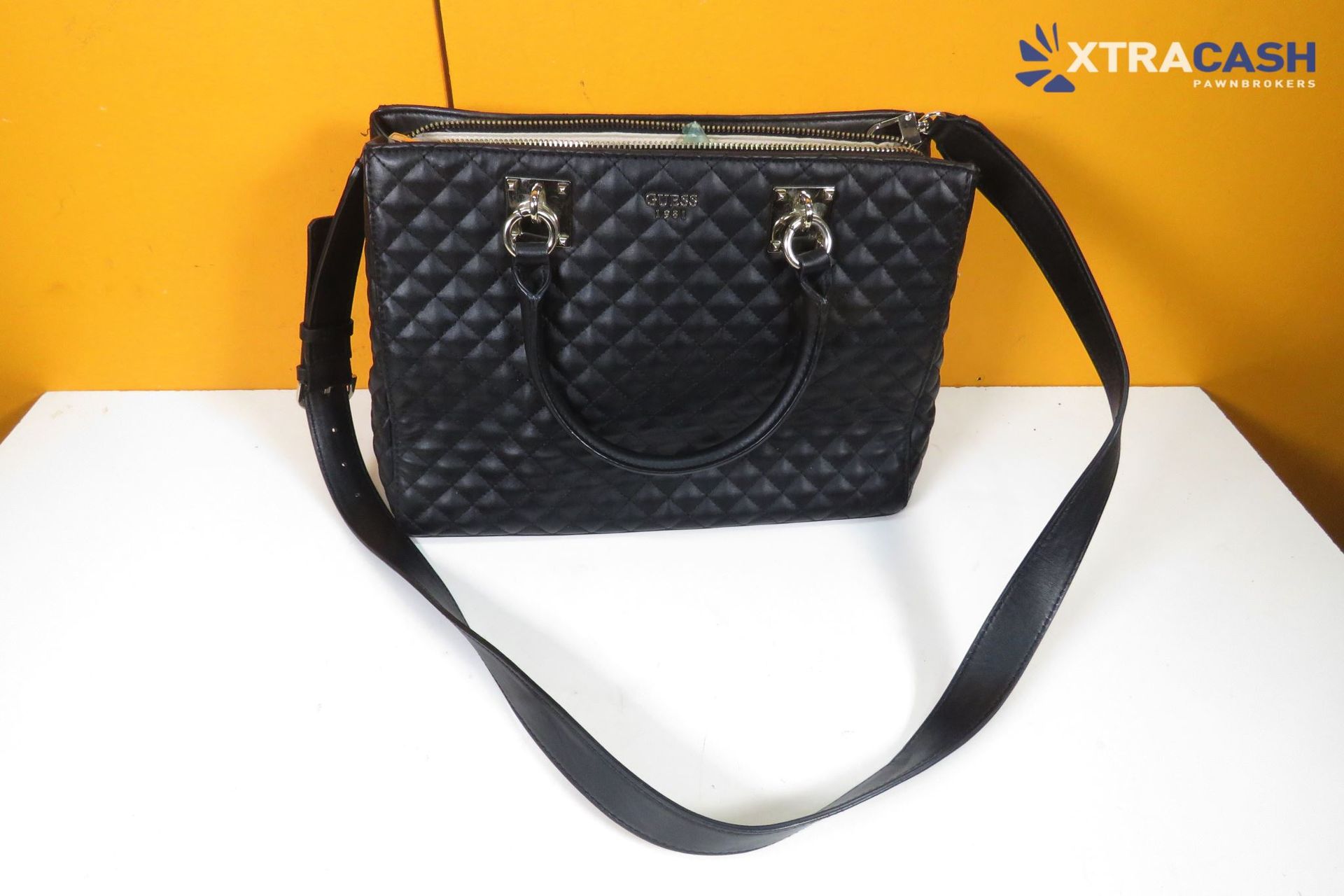 Black quilted handbag with shoulder strap on a white surface against an orange background.