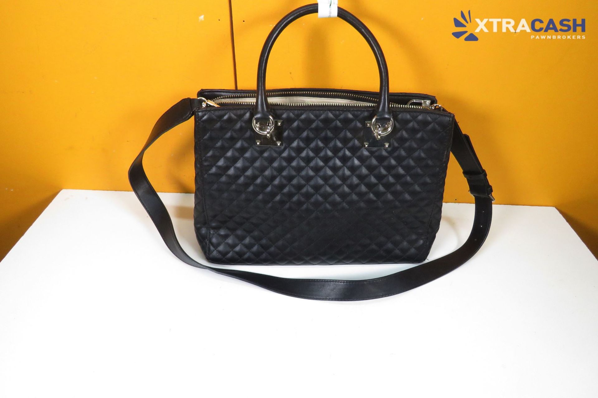 Black quilted handbag with shoulder strap on a white surface against an orange background.