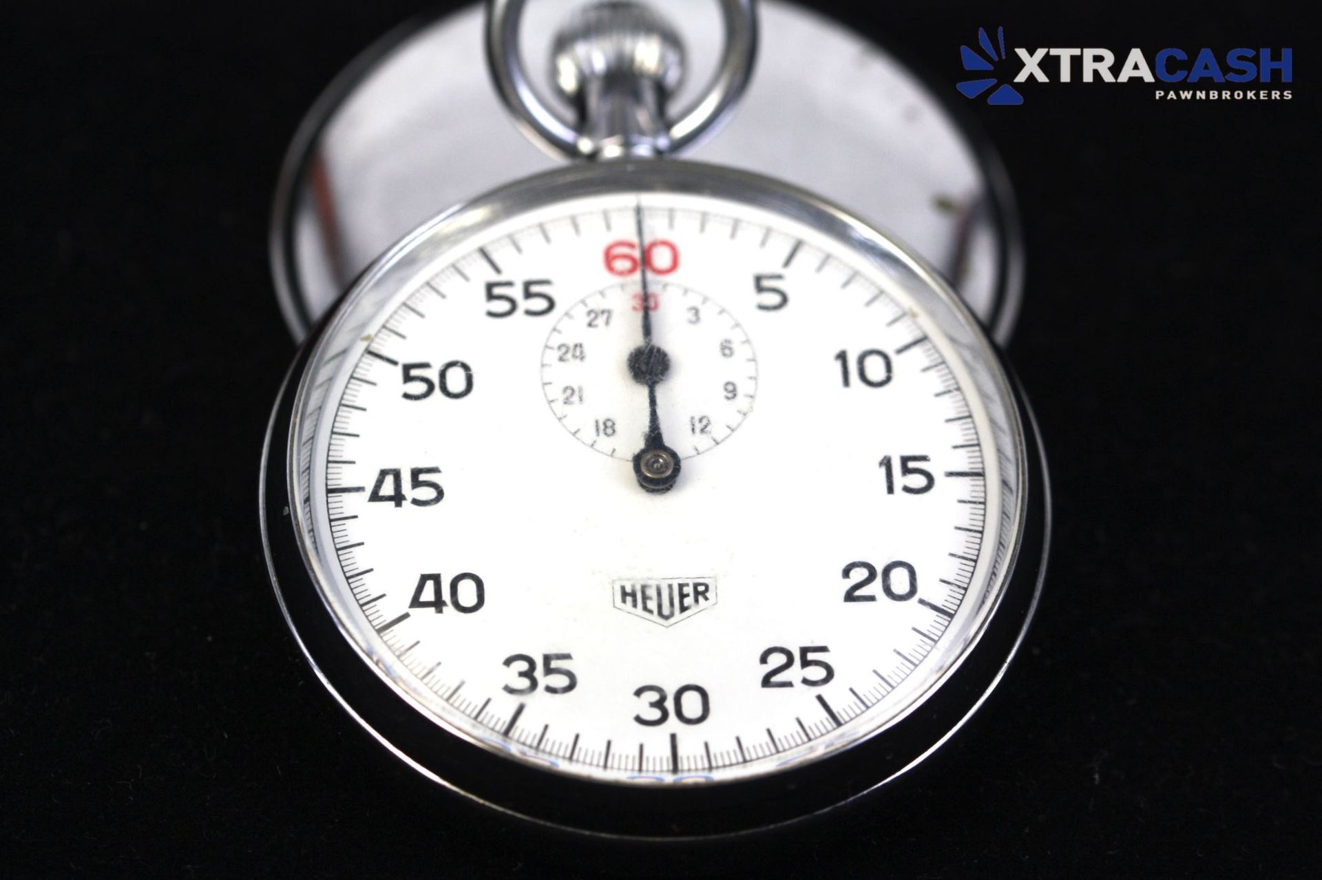 Close-up of a white Heuer stopwatch with black numerals and a red 60-second marker on a dark background