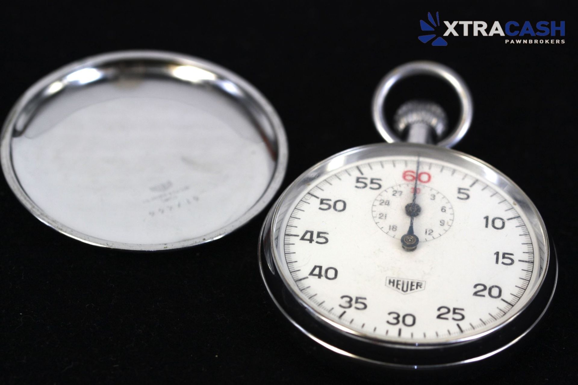 Close-up of a white Heuer stopwatch with black numerals and a red 60-second marker on a dark background