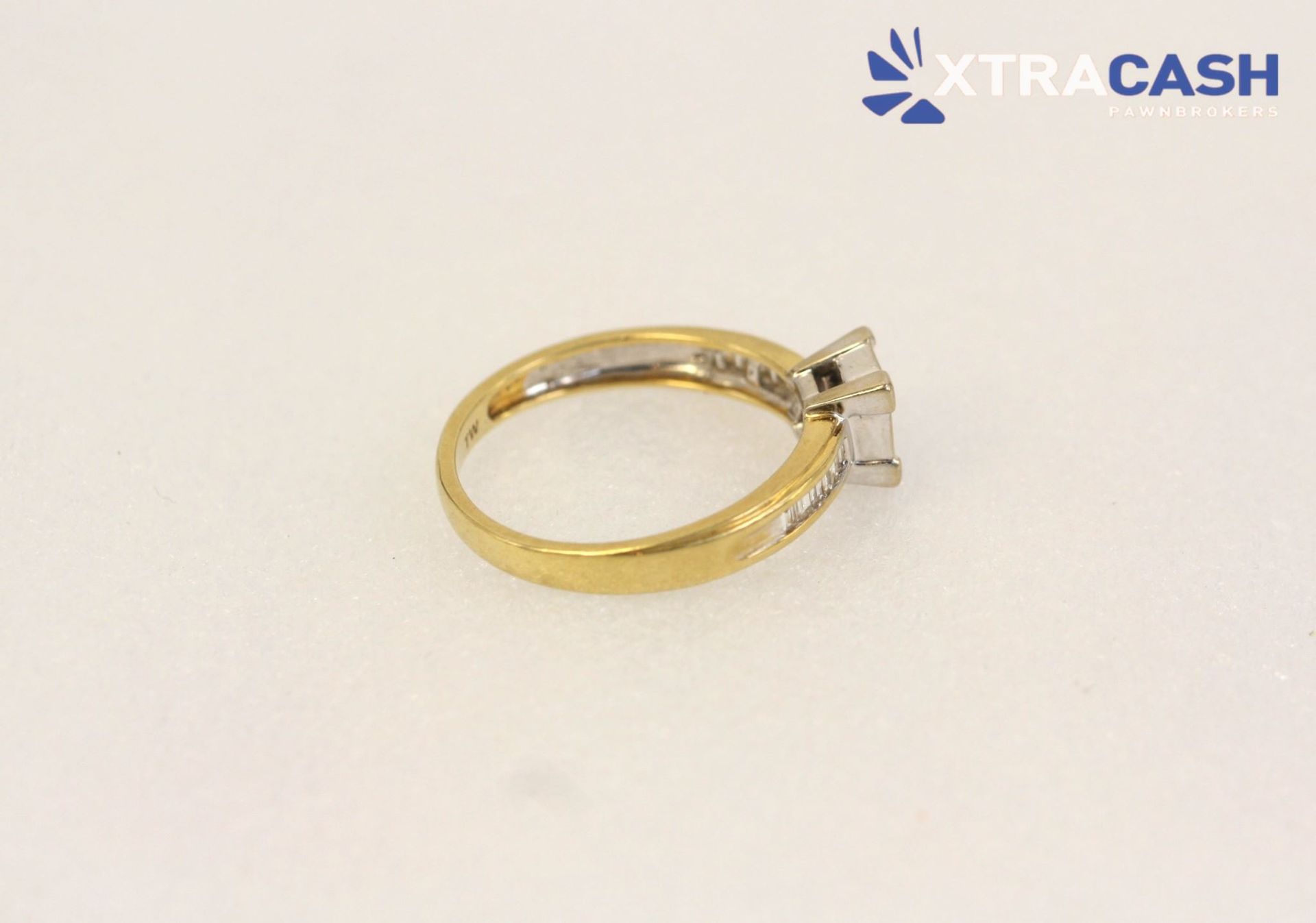 Gold ring with square diamond setting and small side stones on a white background