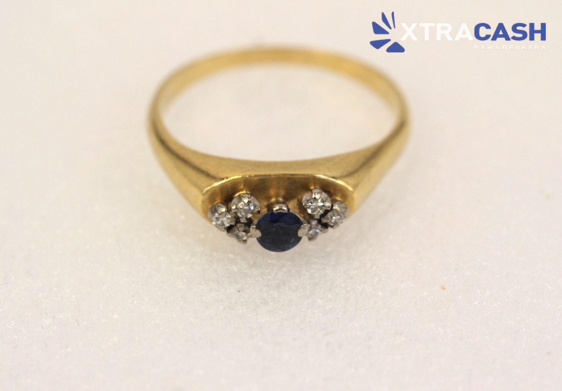 Gold ring with a dark blue gemstone and small clear stones on a white background