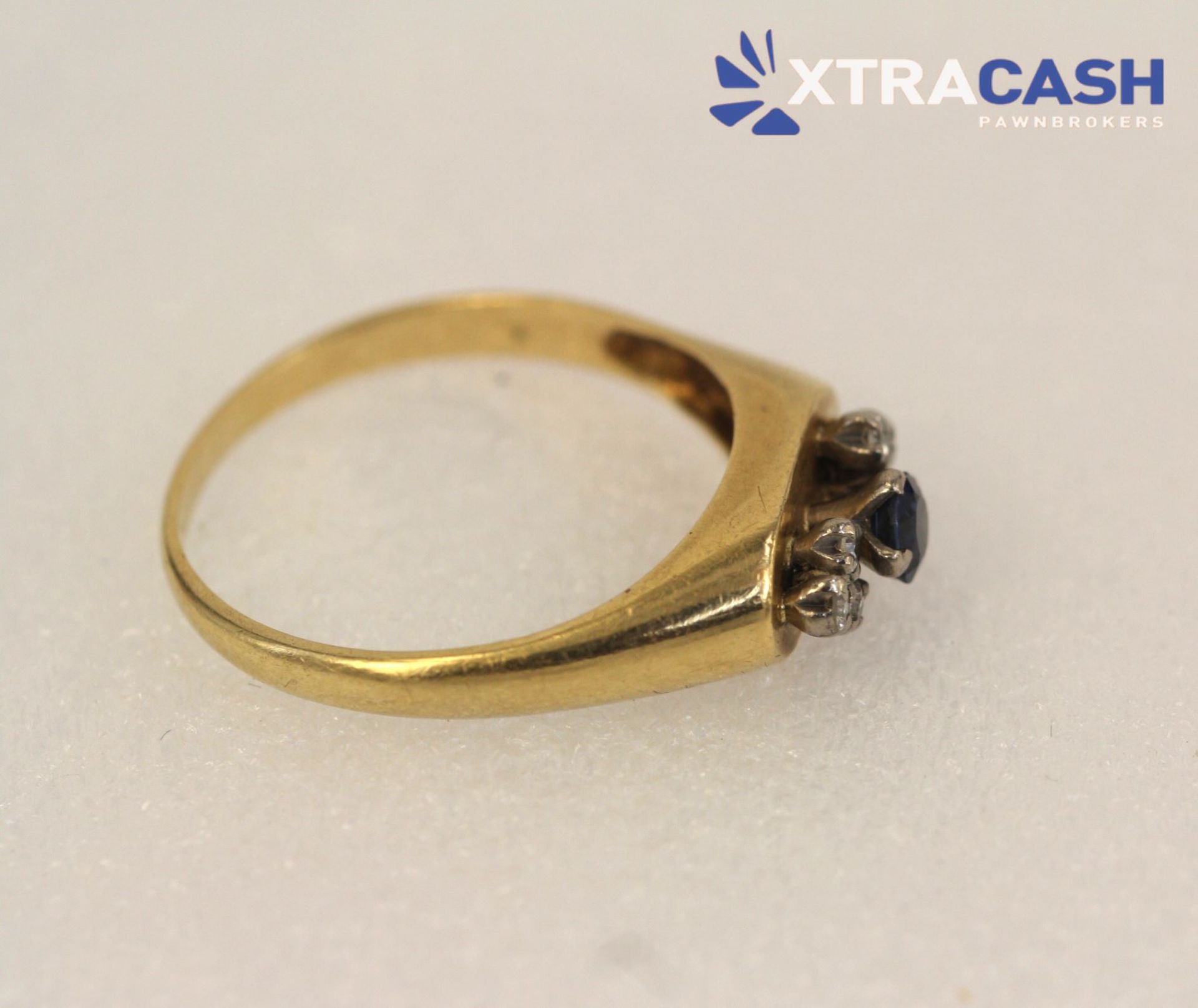 Gold ring with a dark blue gemstone and small clear stones on a white background