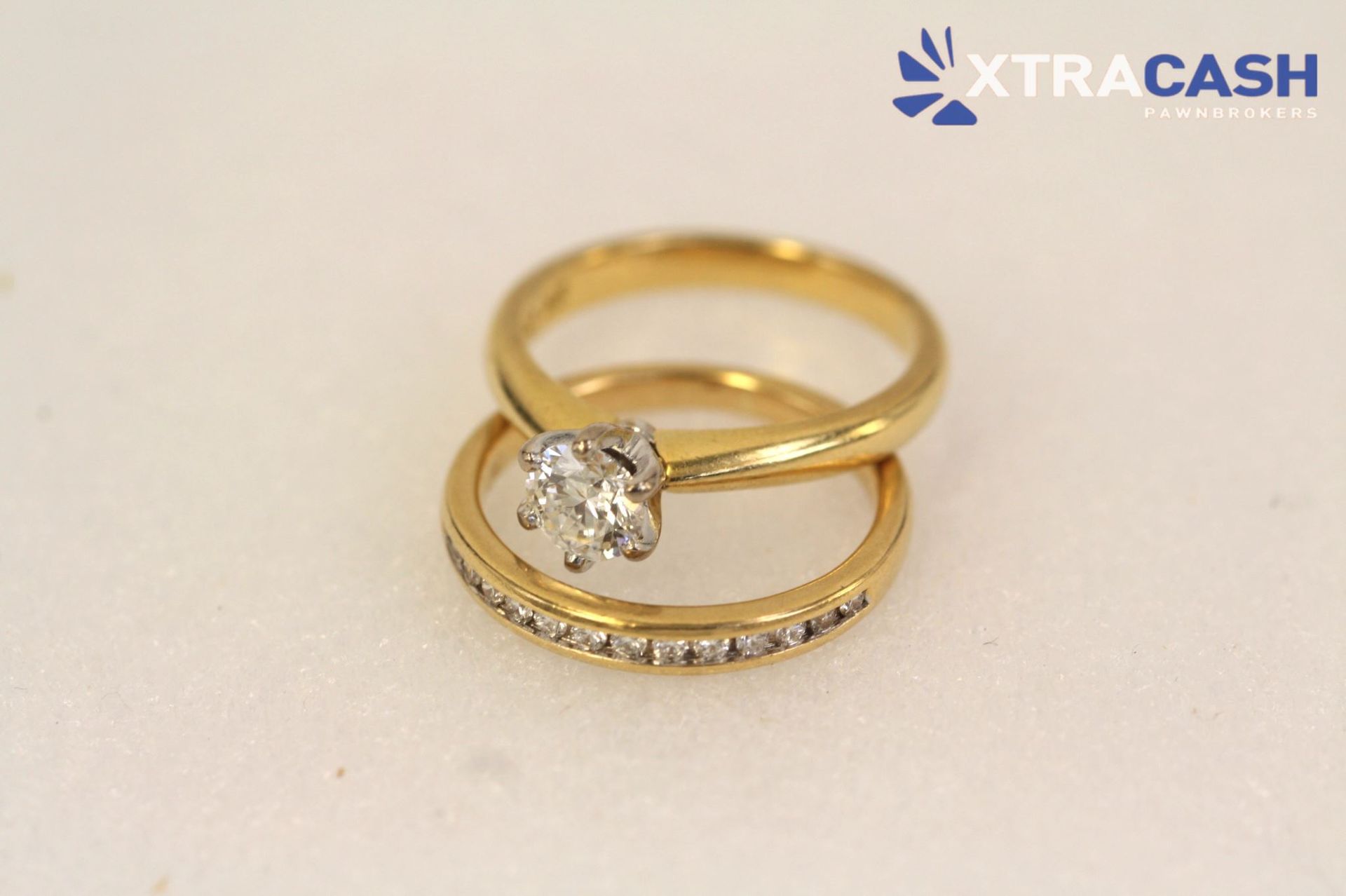 Two gold rings with a solitaire diamond and pavé band on a light background