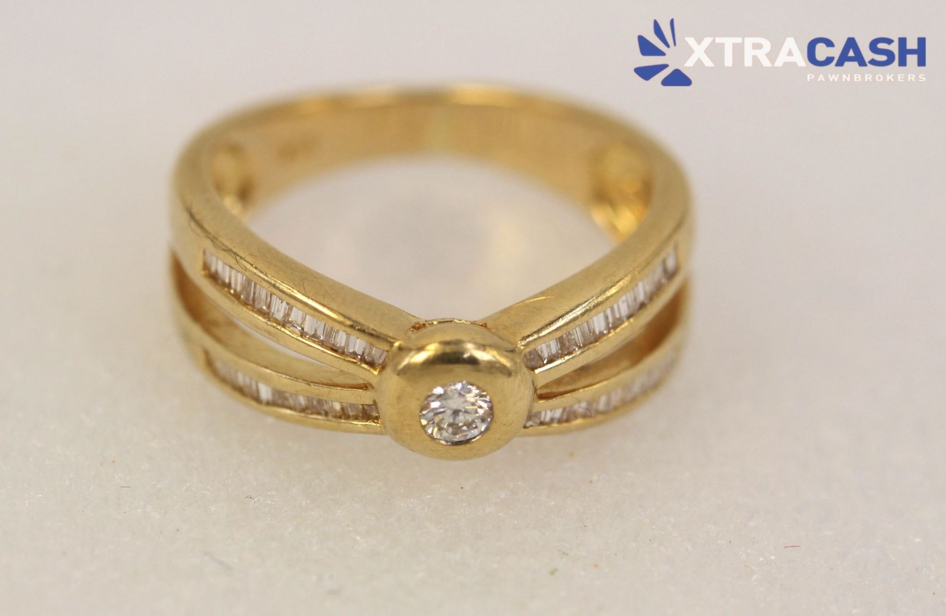 Gold ring with a central clear gemstone and double band details on a light background