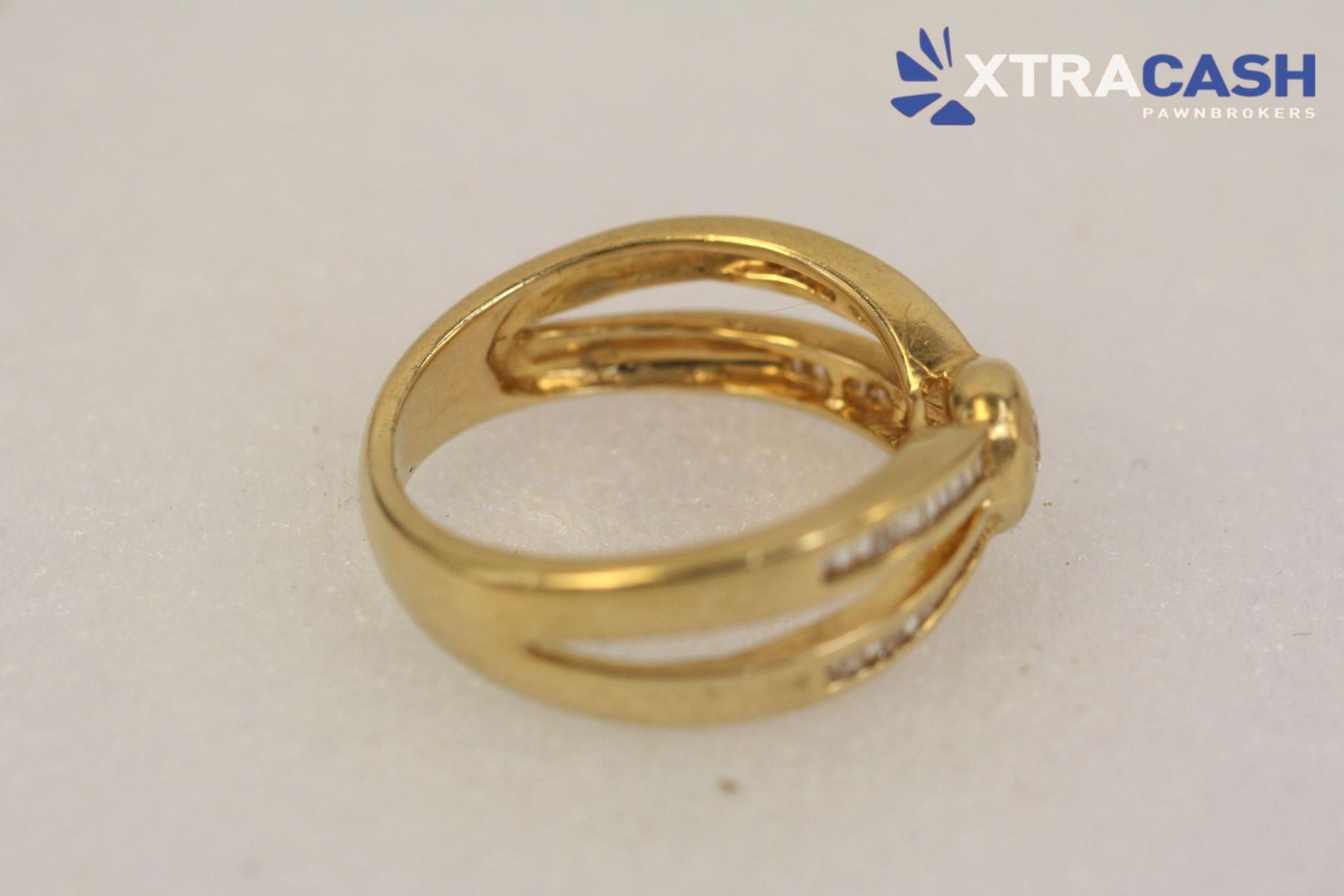 Gold ring with a central clear gemstone and double band details on a light background