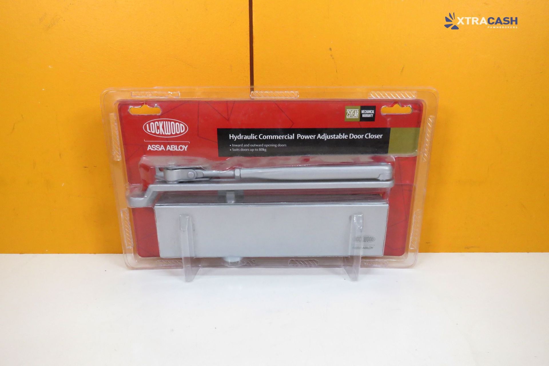 Red and gray wallet in clear packaging on a white surface against an orange wall.