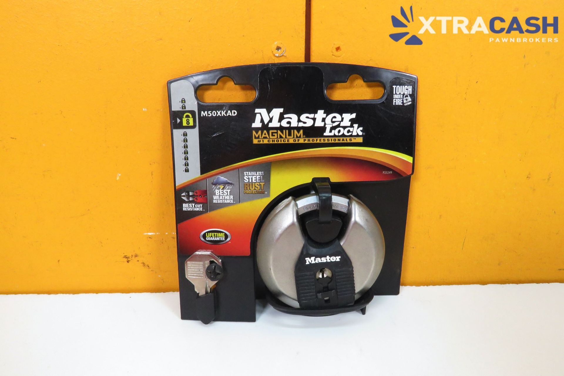 Packaged black and silver Master Lock cable lock on an orange background, with XTRACASH watermark.