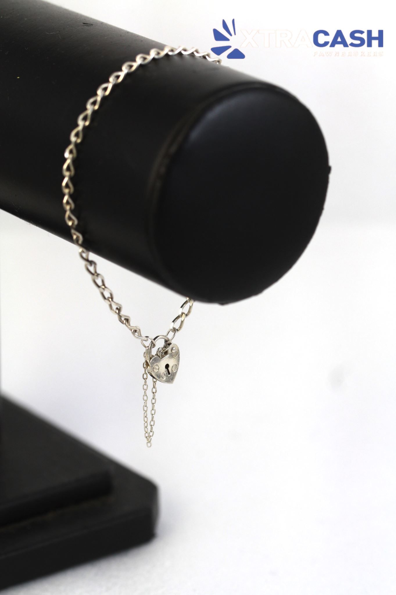 Silver necklace with heart pendant draped over a black display stand, with