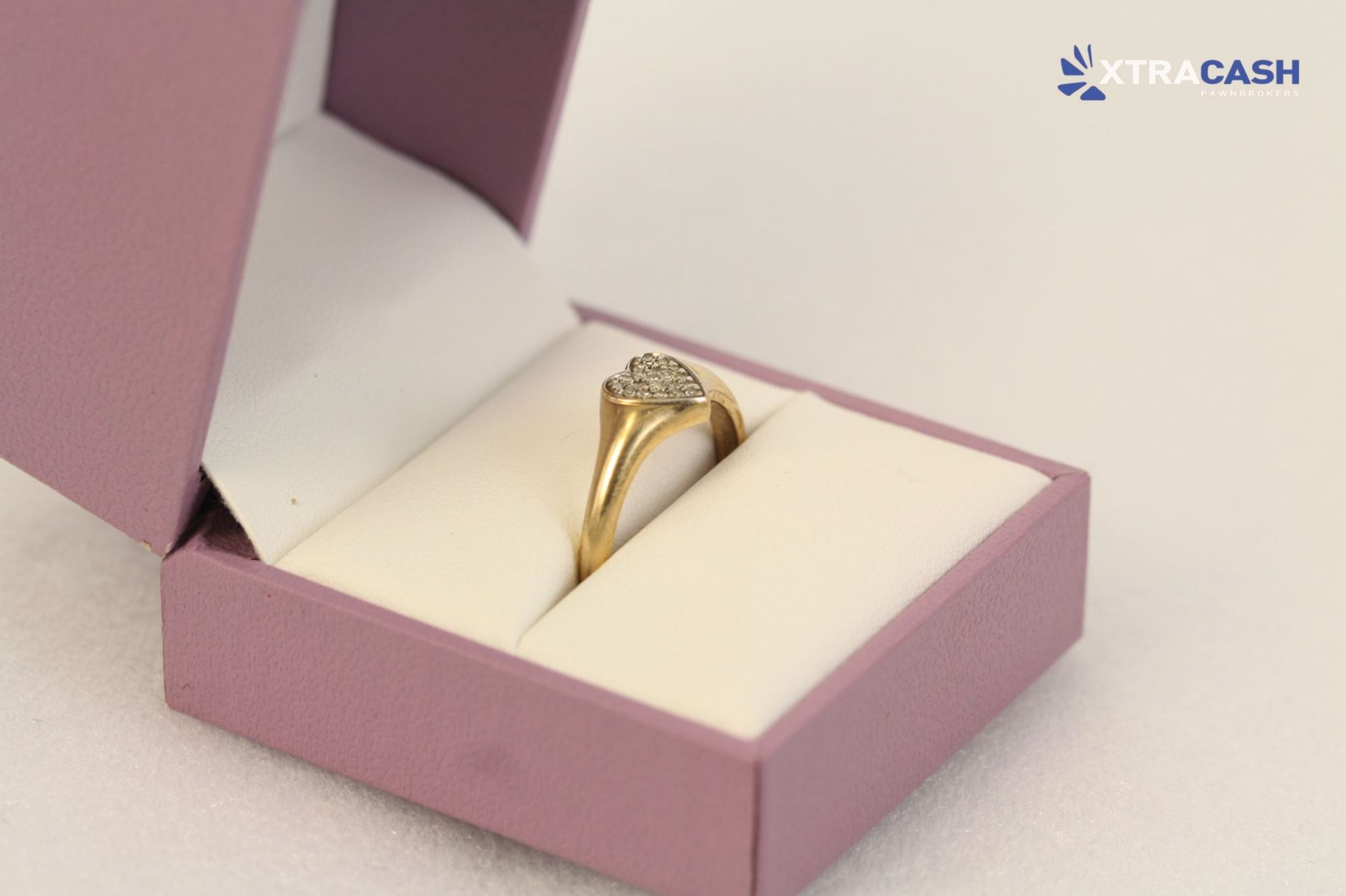 Gold ring in a pink jewelry box with a diamond on a soft white cushion
